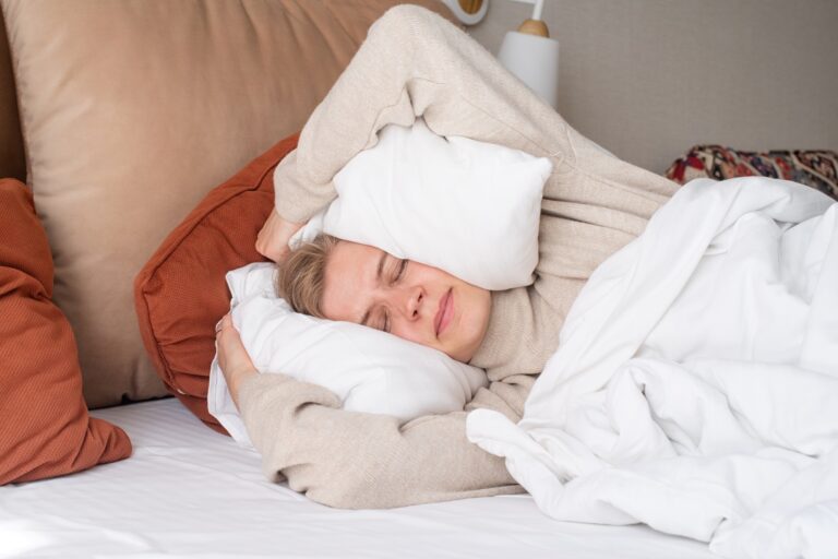 Woman sleeping at bed at home, covering ears with pillows from noise
