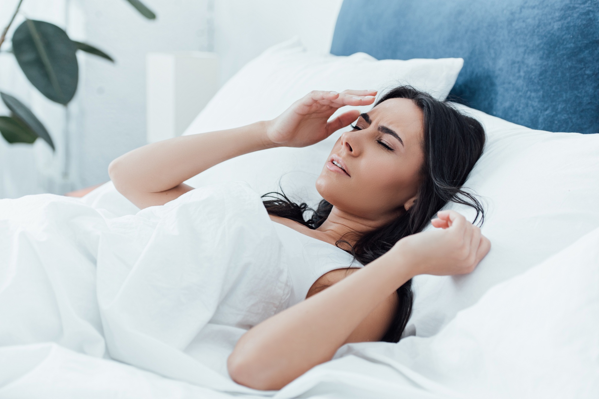 Irritated brunette woman lying in bed with closed eyes