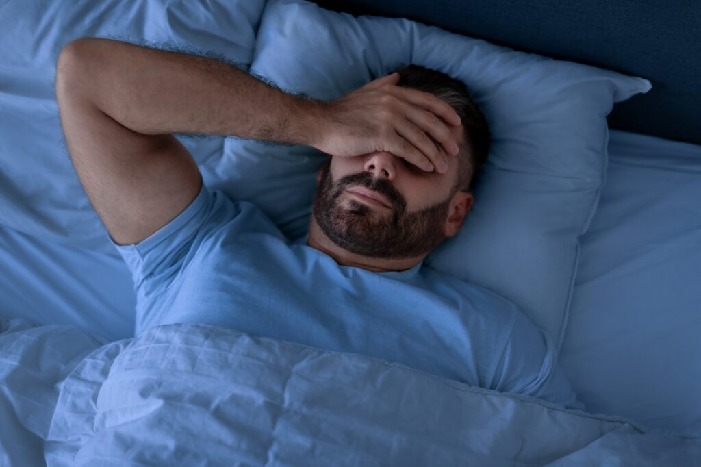 Man Covering Face With Hand Lying Not Sleeping In Bedroom