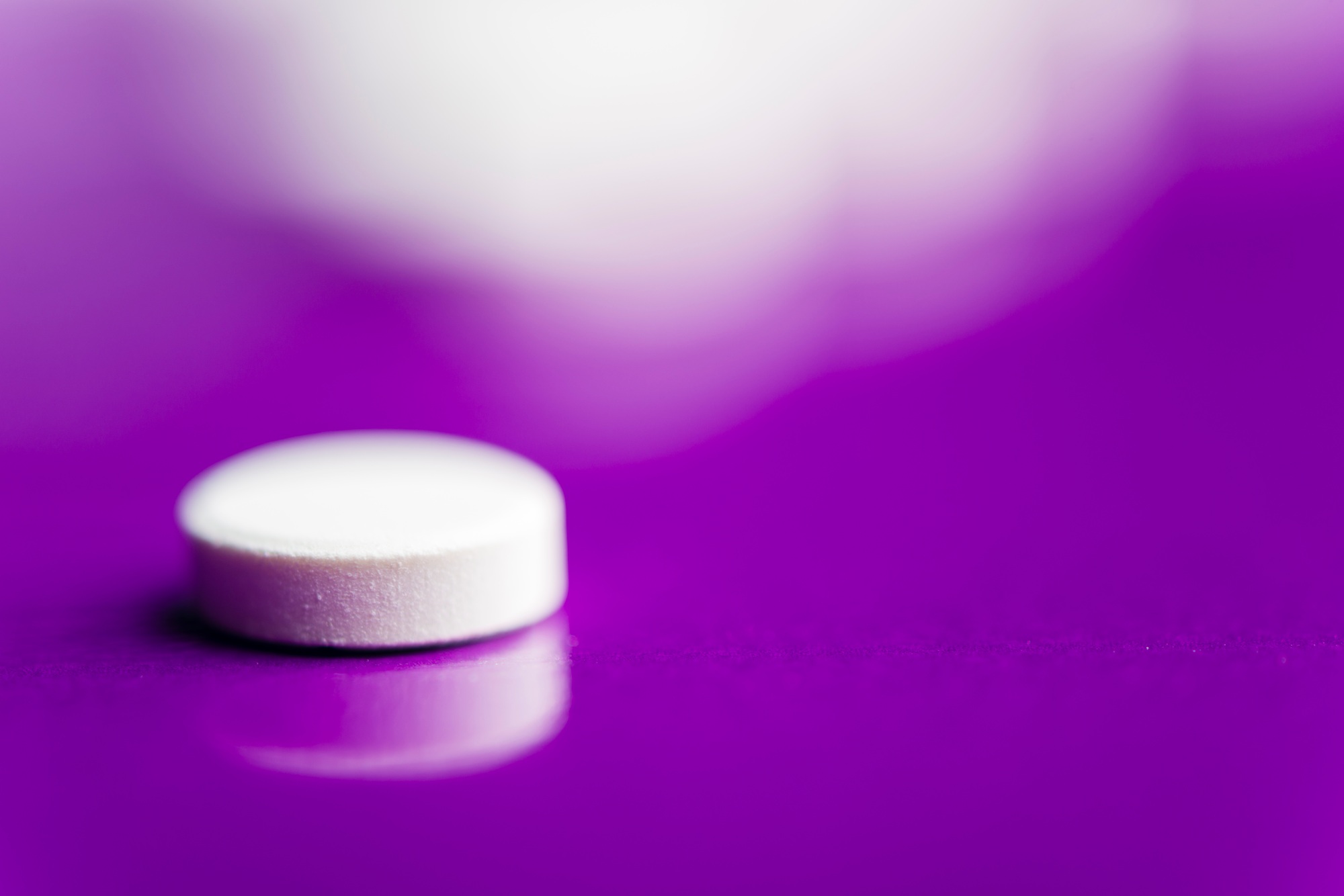 White pills over a solid lilac background with reflection and blurred pills behind.