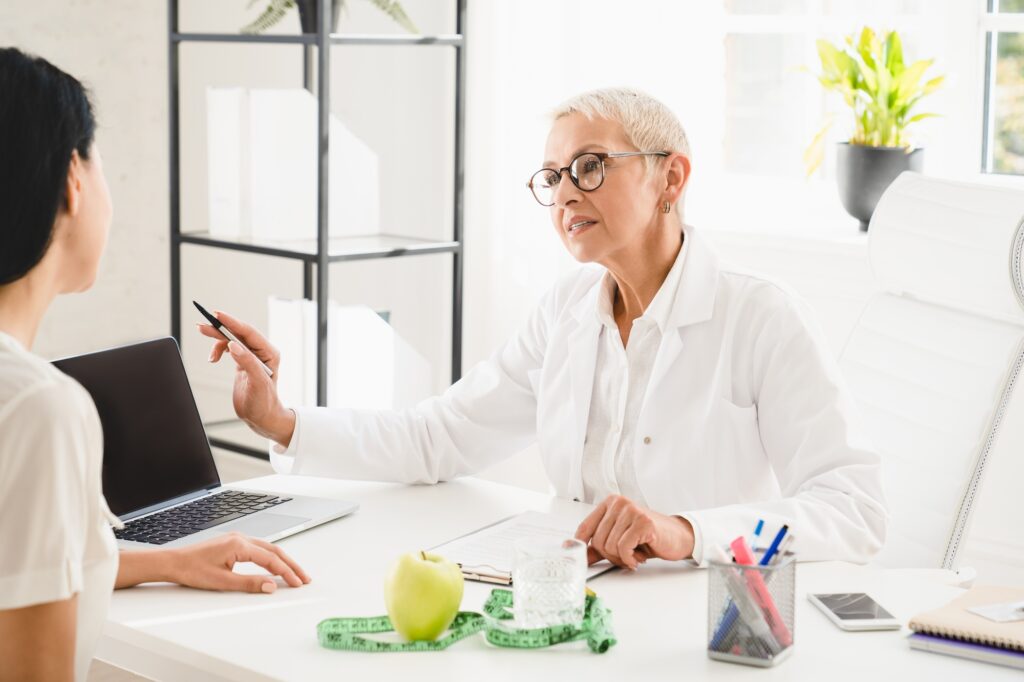 Nutritionist dietitian explaining to female patient weight loss nutrition. Mockup laptop screen